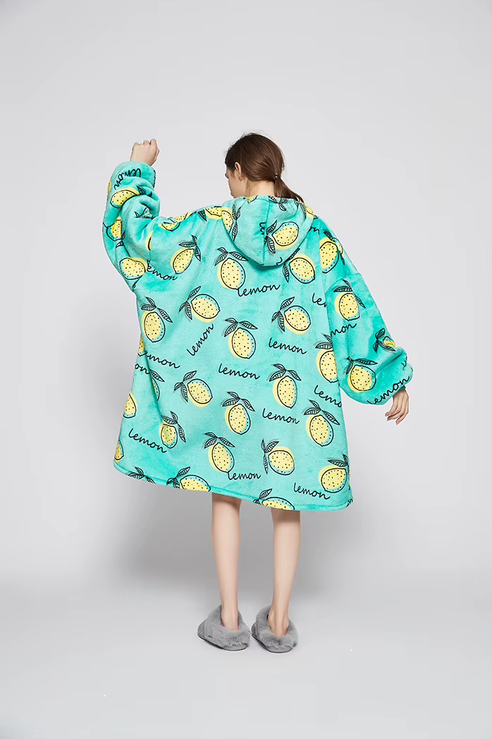 Back view of a model wearing the Lemon Squeeze oversized wearable blanket in turquoise with a hand-drawn yellow lemon print and hood up