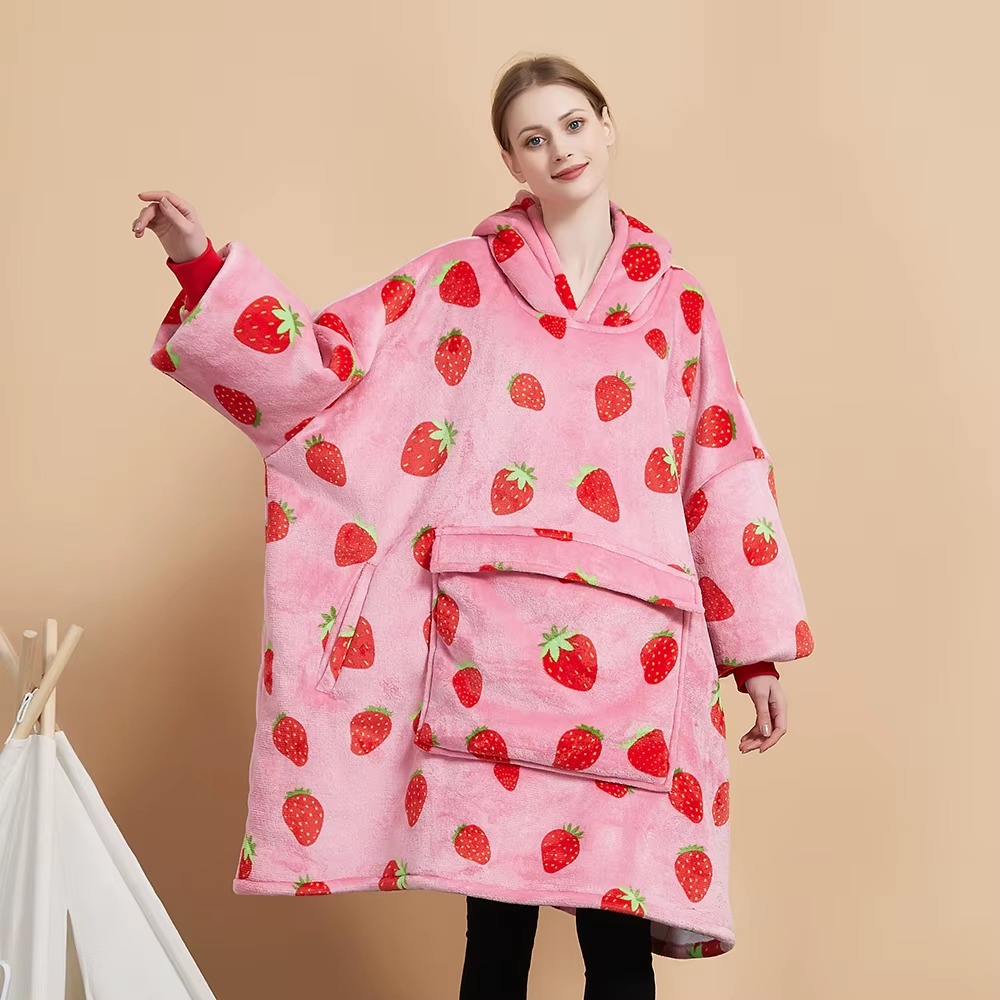 Model wearing the Strawberry Crush oversized wearable blanket in pink with an all-over red strawberry print and a large front pocket