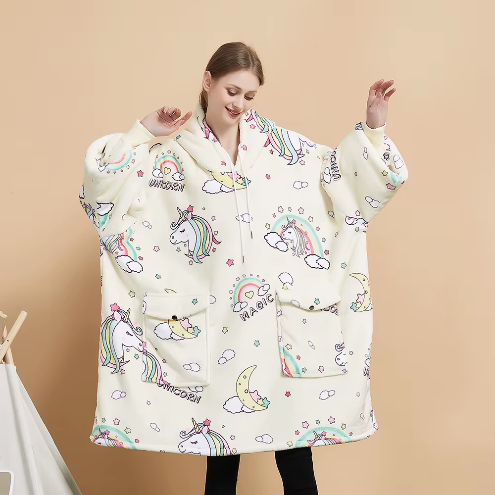 Model wearing the Unicorn Dream oversized wearable blanket in warm ivory with pastel unicorns, rainbows, clouds and moons and two flap pockets